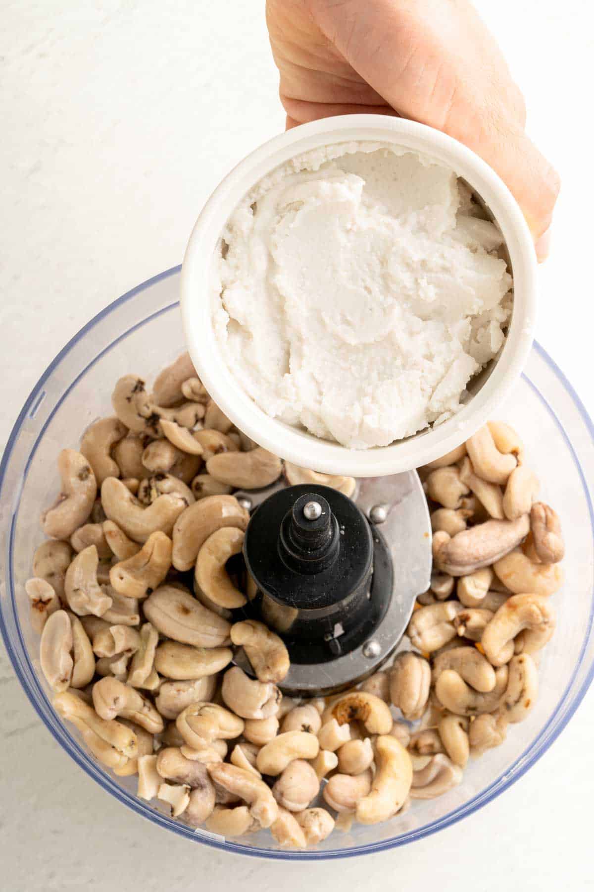 Pouring coconut milk into a in a food processor with cashews.