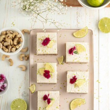 Key lime pie bars on a tray garnished with pink flowers surrounded by ingredients.