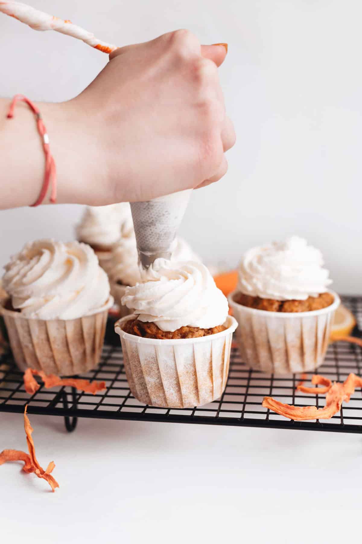 Womans hand applying frosting to carrot cupcakes. 
