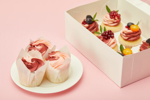 Cupcakes in a box and on a plate with a pink backrgound.