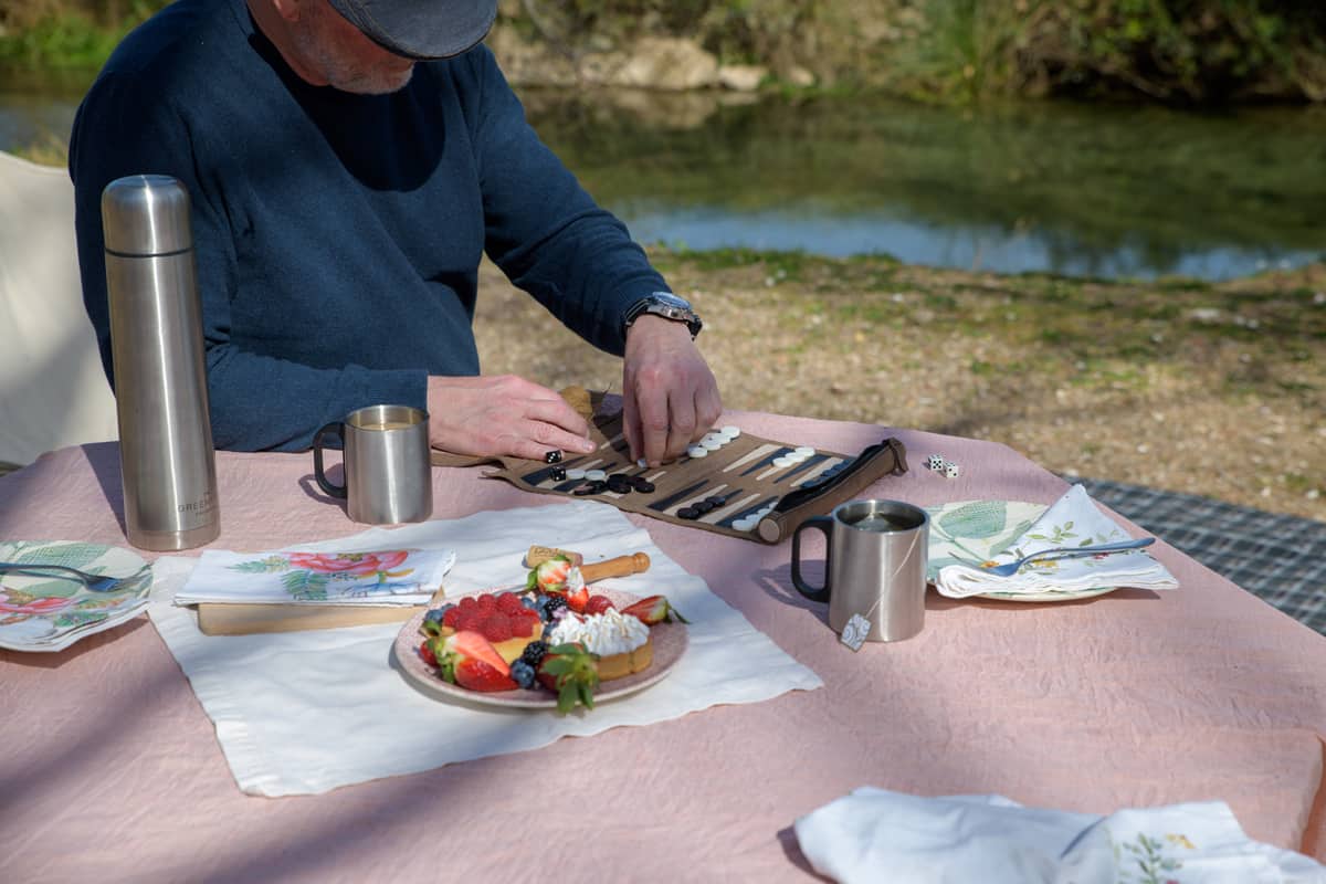 Man playing backgammon at a picnic setting with tea and cakes.