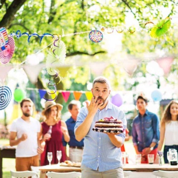Man with a cake on a family celebration or a garden birthday party outside, licking his finger.