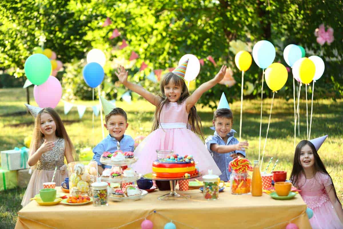 Children celebrating a birthday in the park with lots of decorations and cake. 