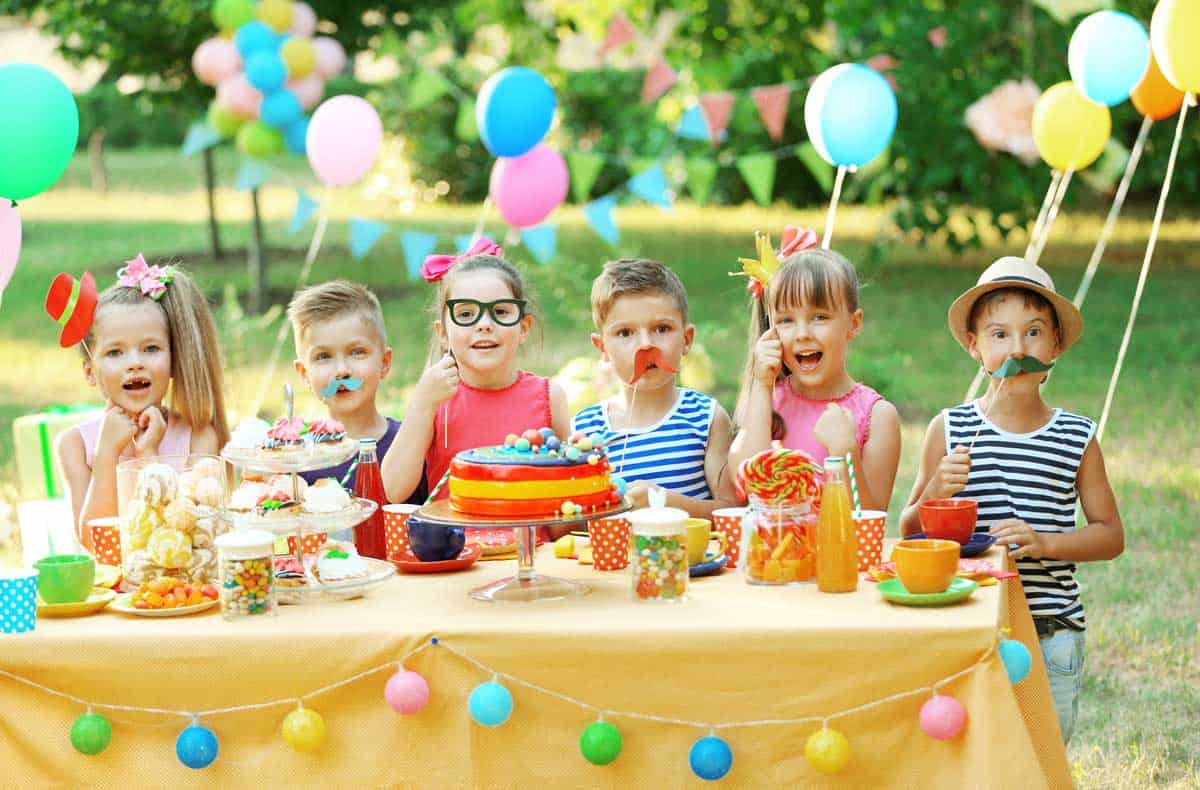 Children celebrating a birthday in the park at a colourfully decorated picnic.