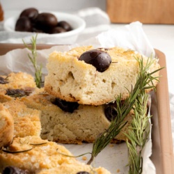 A piece of keto focaccia bread with olives and a rosemary sprig.