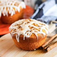 A spiced pumpkin muffin with drizzled glaze on a wooden cutting board.