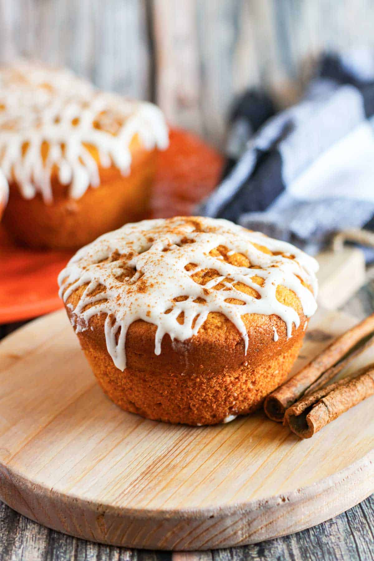 A spiced pumpkin muffin with drizzled glaze on a wooden cutting board.