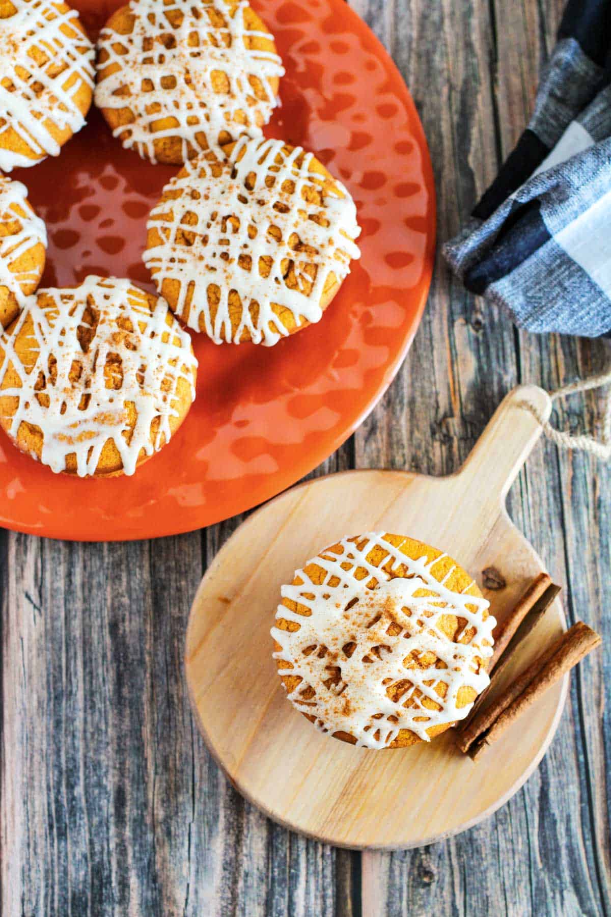 Pumpkin spice muffins with icing and cinnamon sticks on a plate.