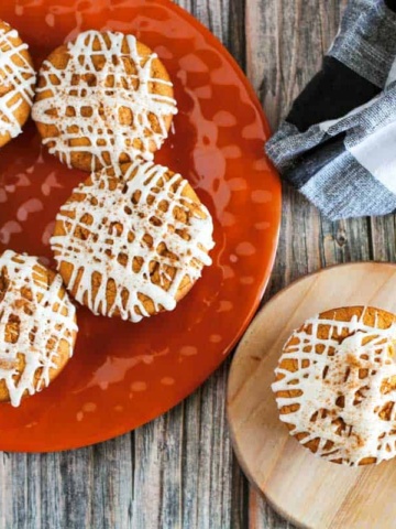 Pumpkin muffins on an orange plate with cinnamon sticks.