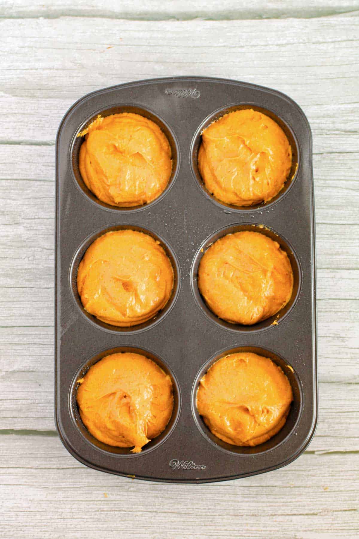 Pumpkin muffin batter in a muffin tin.