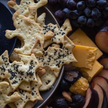 A plate of cheese, crackers and grapes on a black plate.