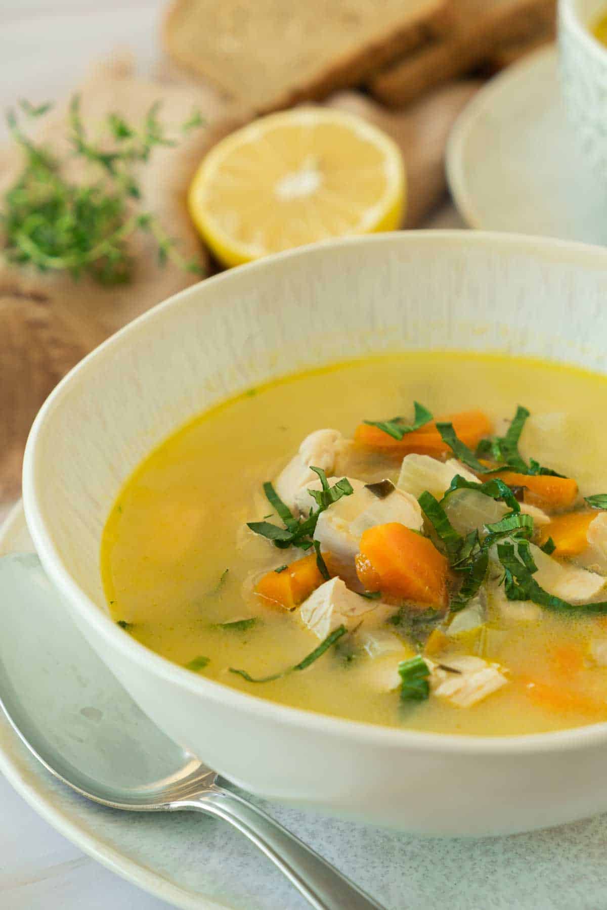 A bowl of chicken soup with carrots and lemons.