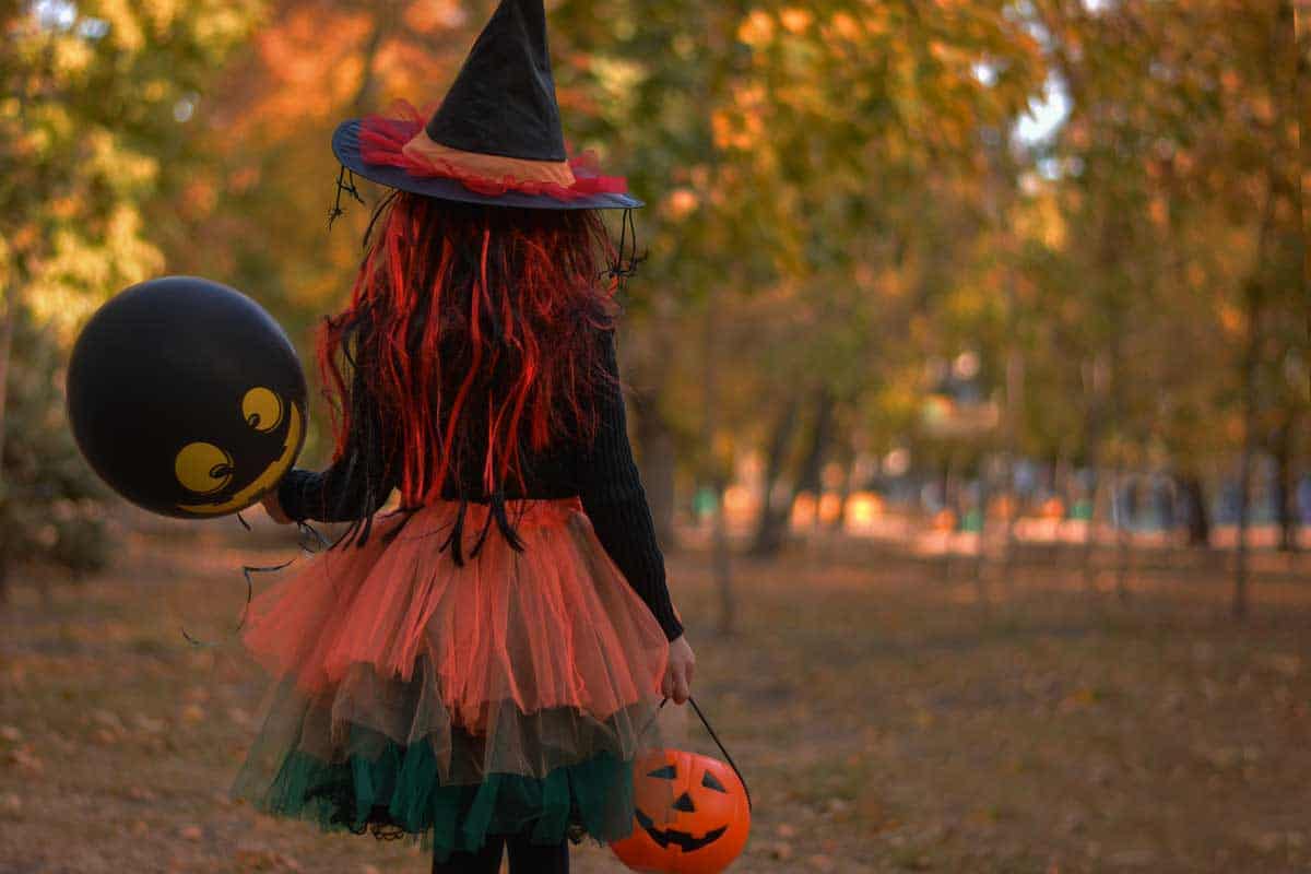 A girl in a witch costume holding a balloon in the park.