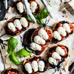 A plate of bruschetta with black olives, tomatoes and basil.