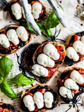 A plate of bruschetta with black olives, tomatoes and basil.