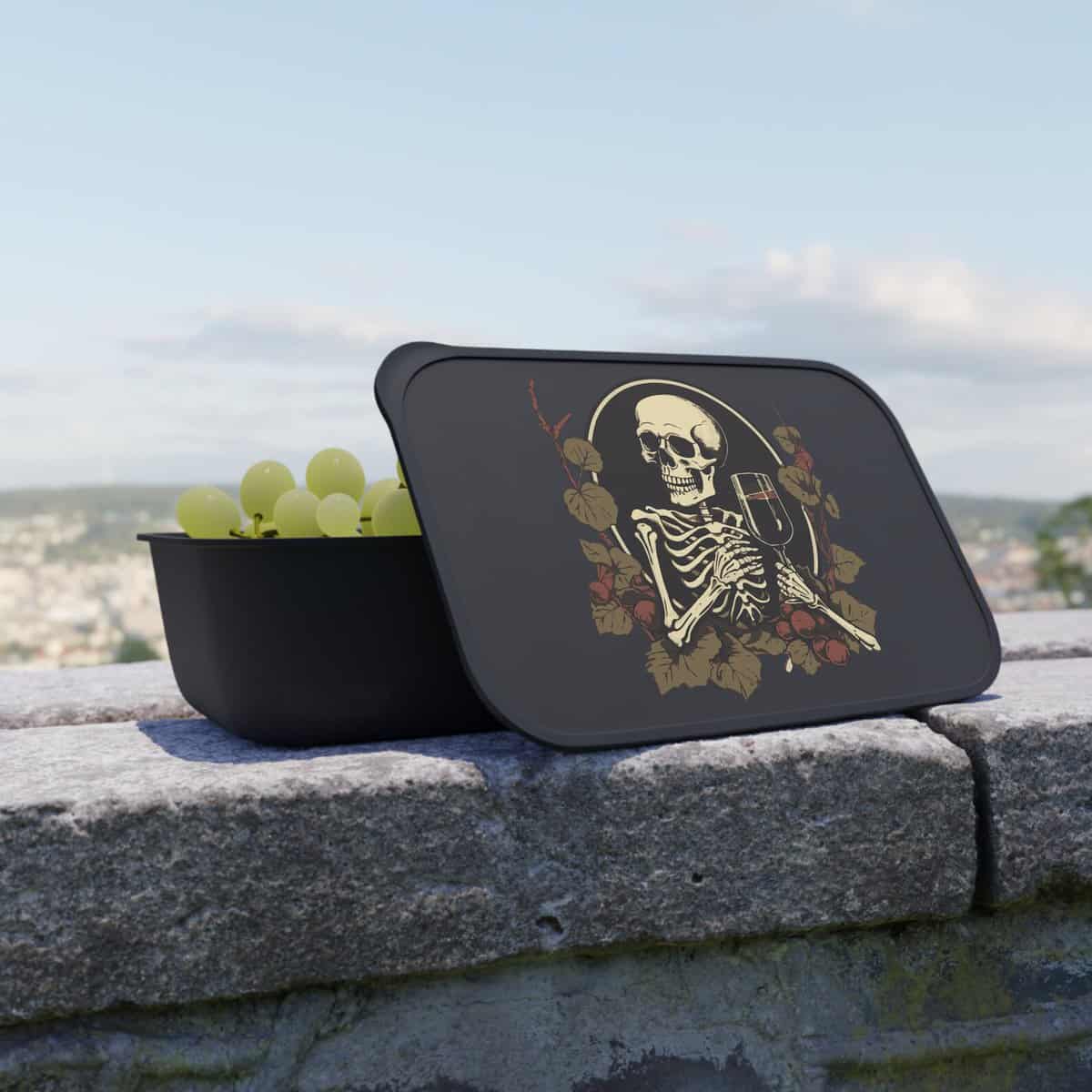 A black lunch box with a skeleton on it and grapes.