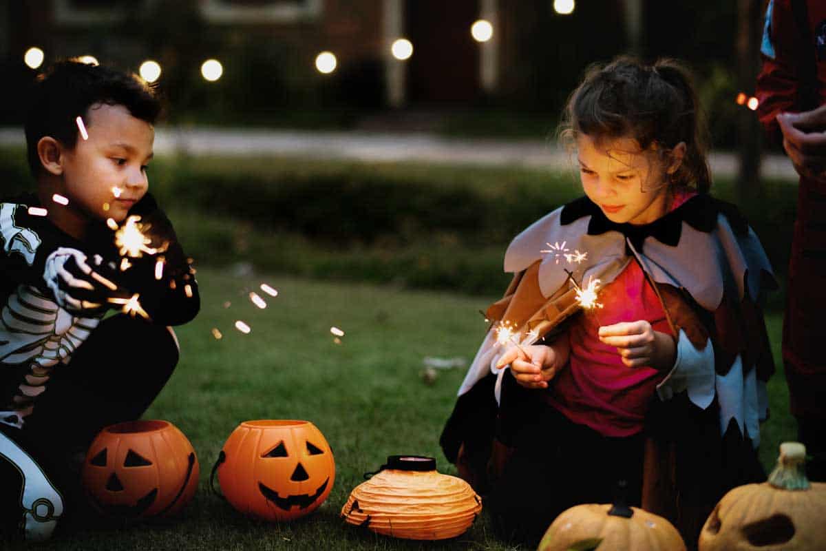 A group of children sitting on the ground with sparklers and pumpkins.