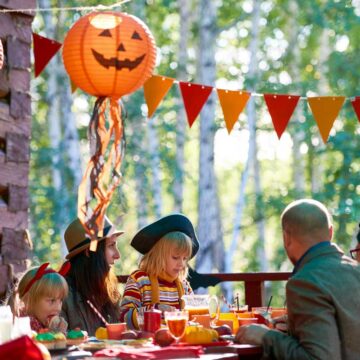 A group of people sitting around a table at a halloween picnic party.