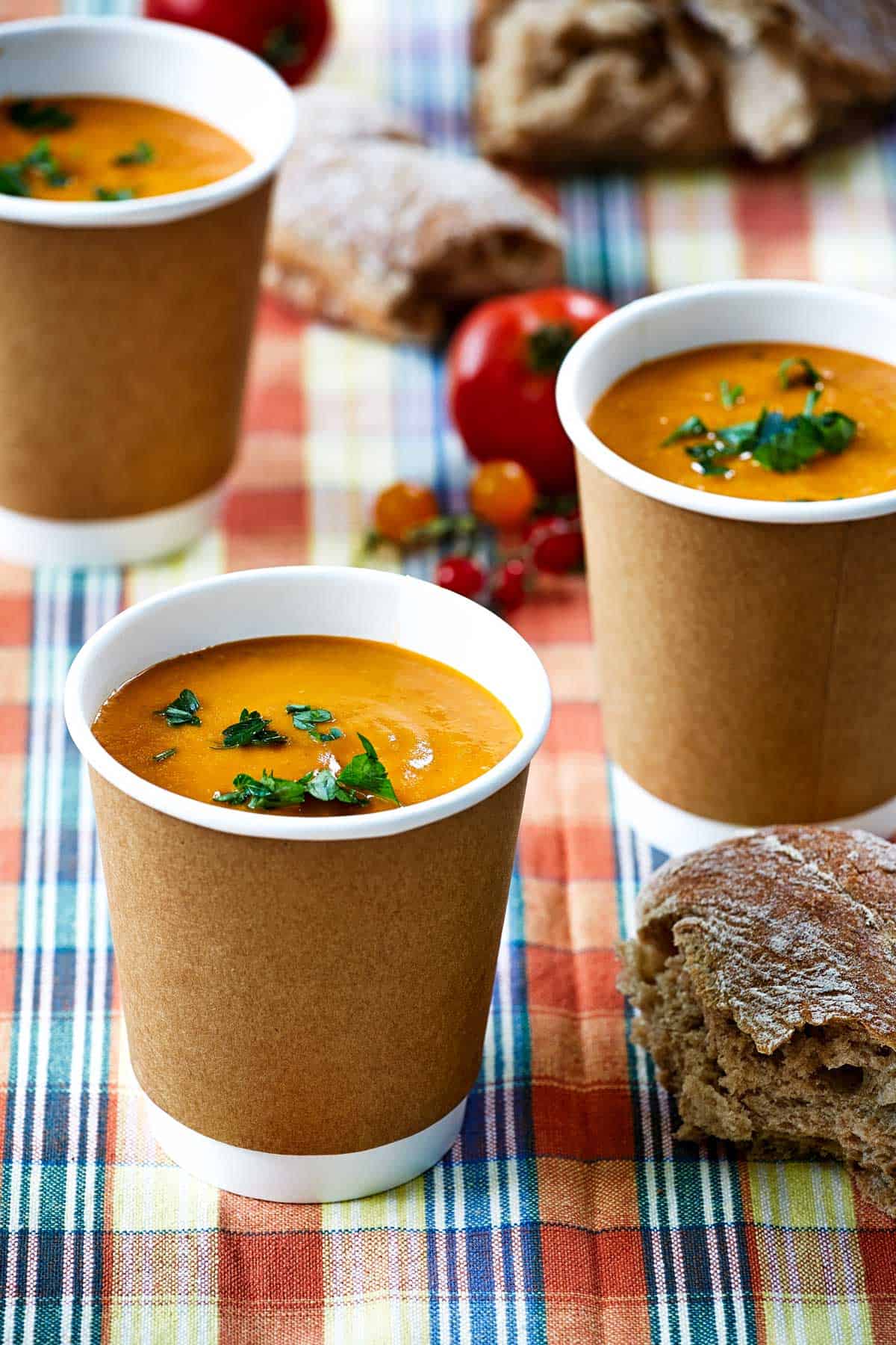 Three cups of soup on a picnic table.