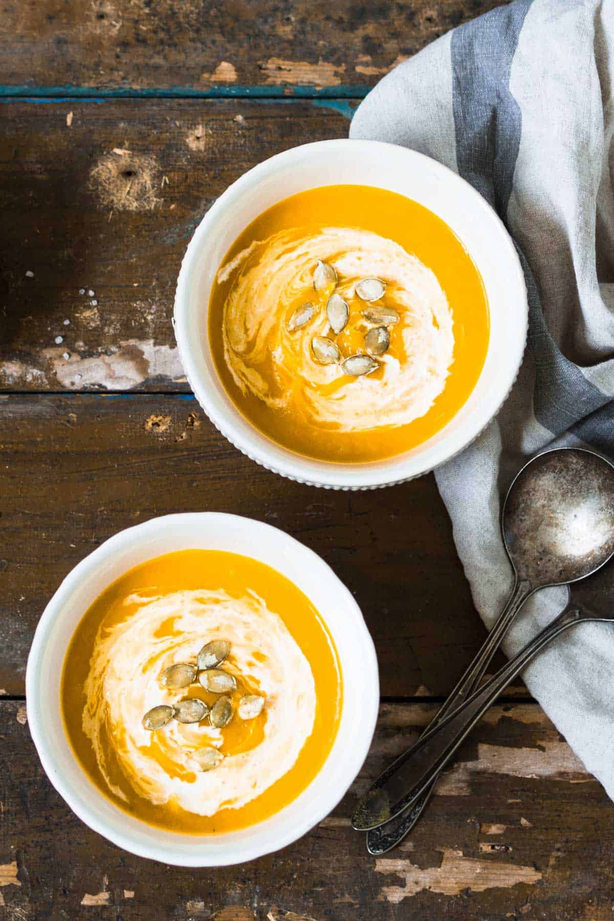 Two bowls of pumpkin soup on a wooden picnic table.