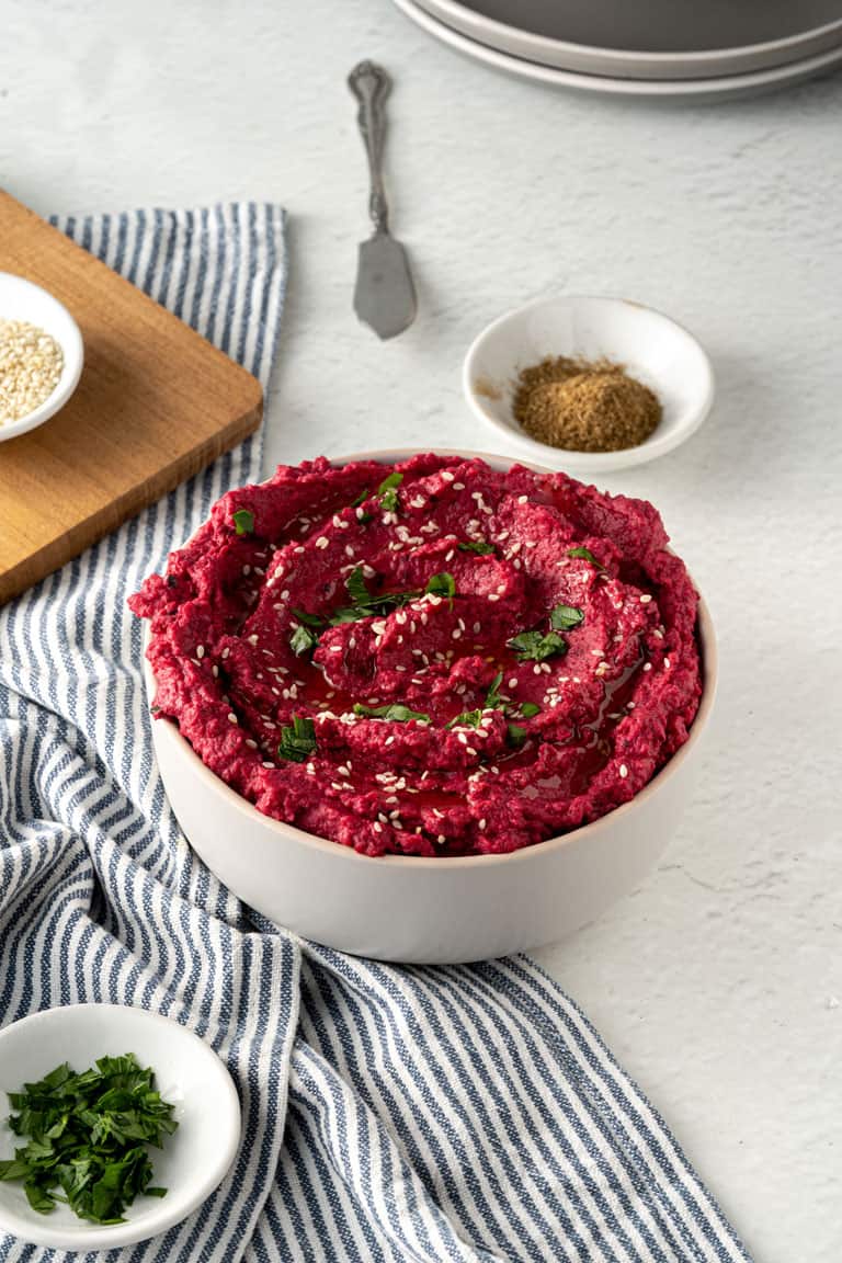 Beet hummus in a bowl with herbs and spices.