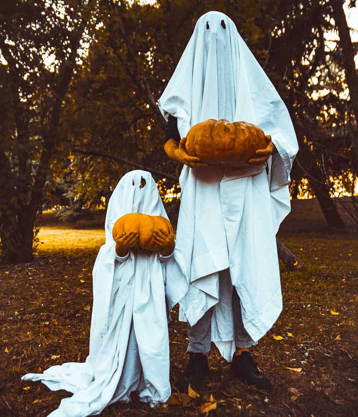 A couple dressed up as ghosts holding pumpkins.