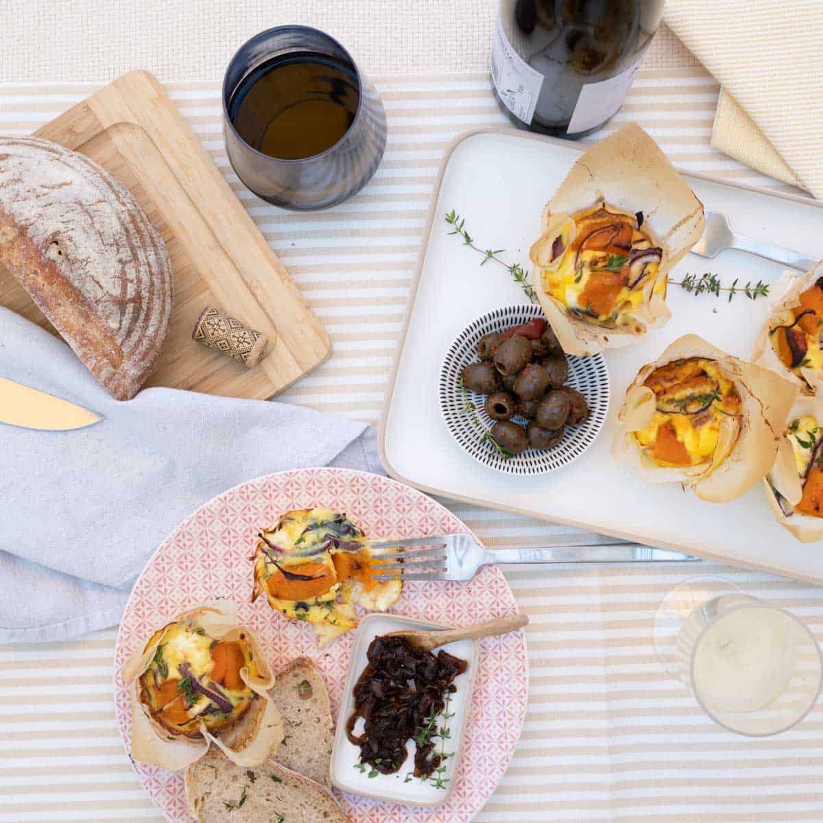 pumpkin frittata's on a striped tablecloth with assorted picnic food and wine.