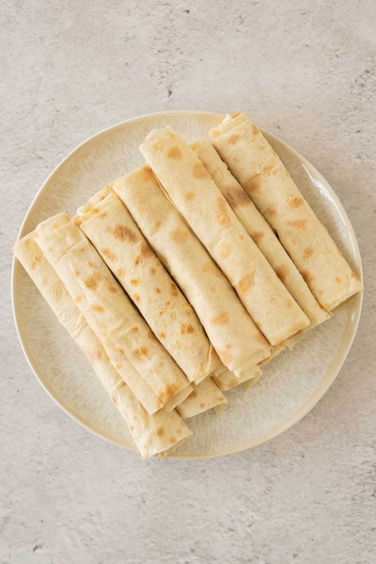 A plate with a stack of uncooked cheese pastry rolls.