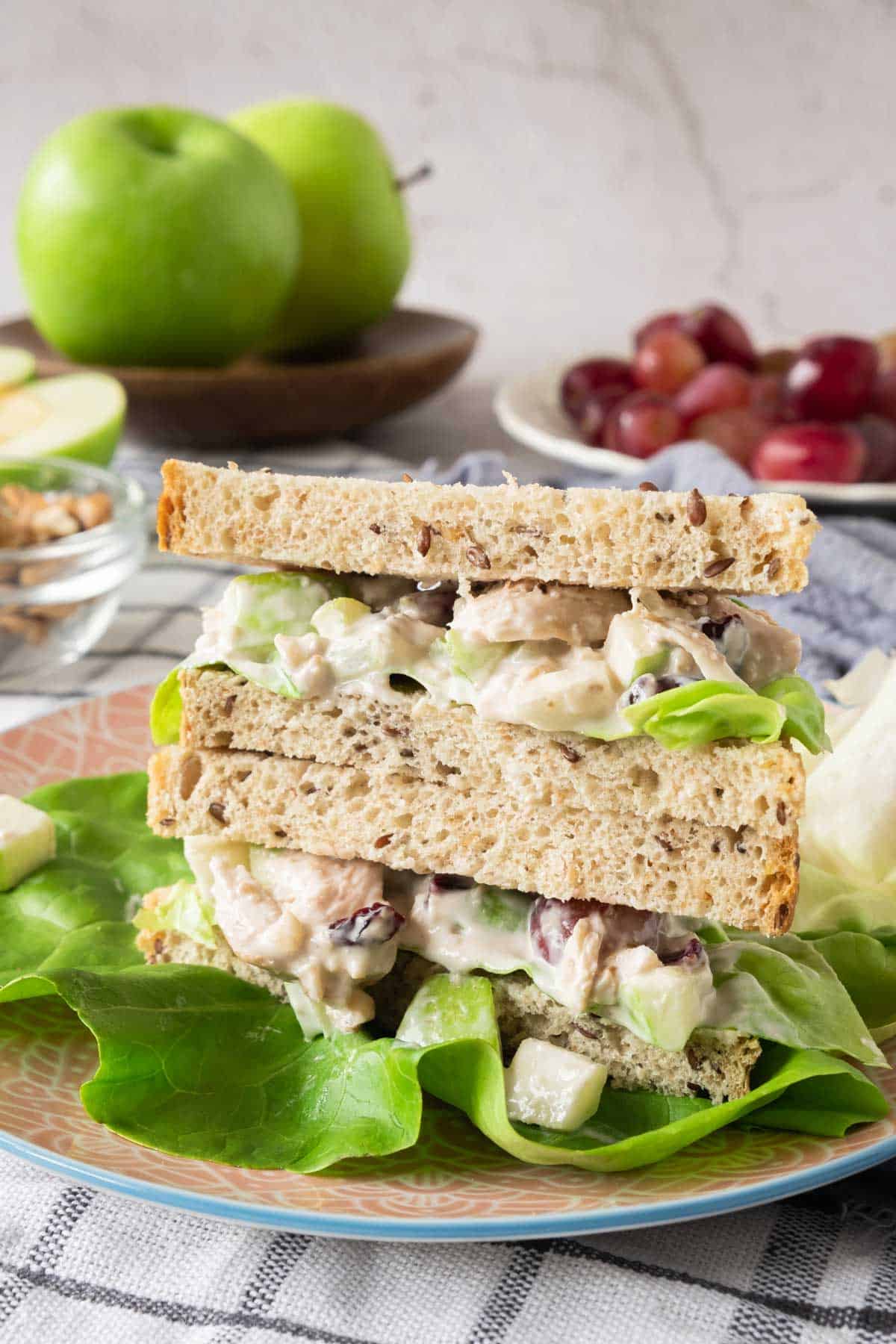 A Waldorf chicken salad sandwich on a plate with apples and grapes.