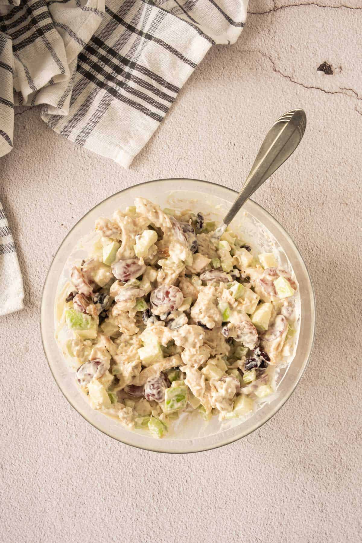 A bowl of Waldorf chicken salad on a table next to a napkin.