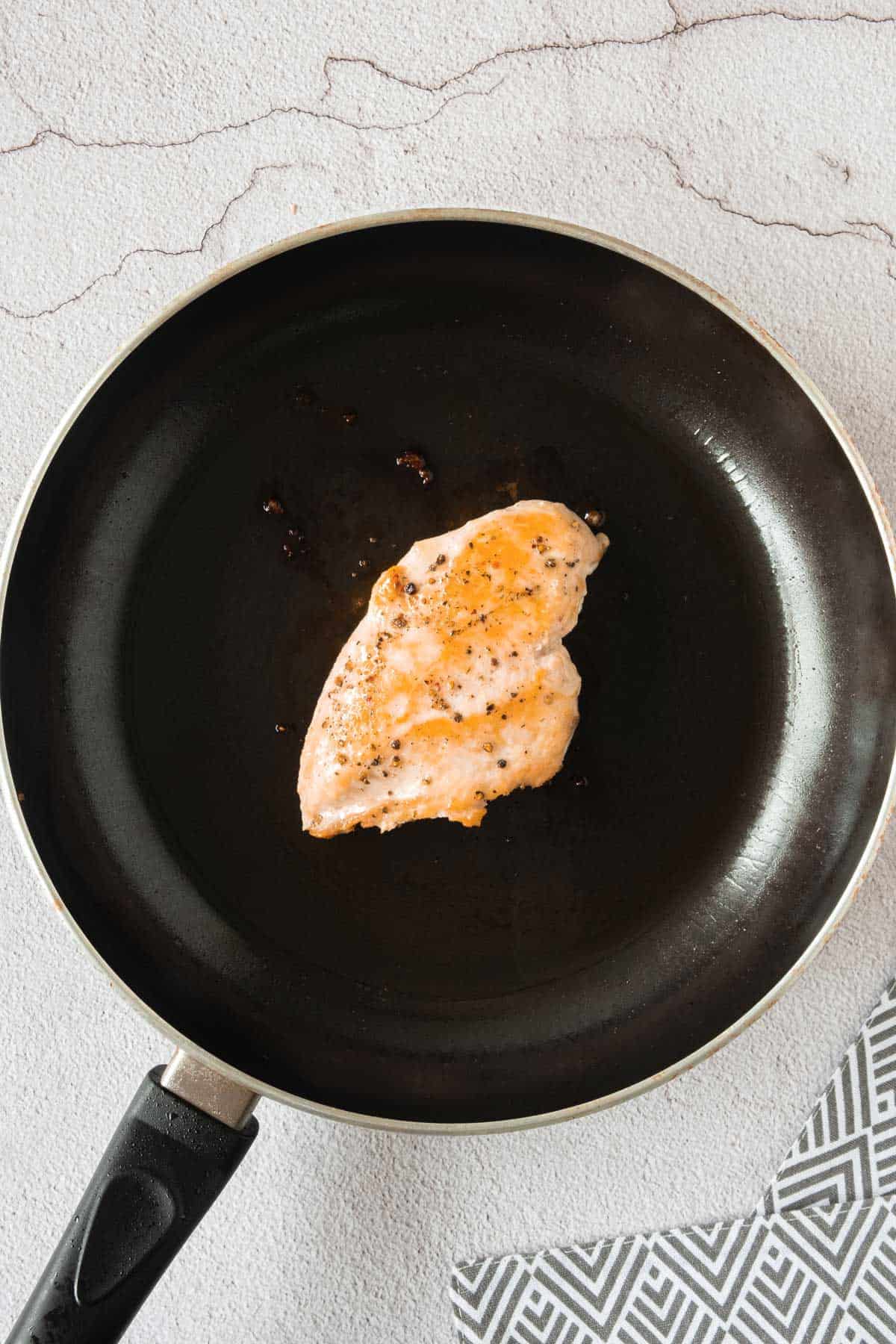 A piece of chicken is being cooked in a frying pan.