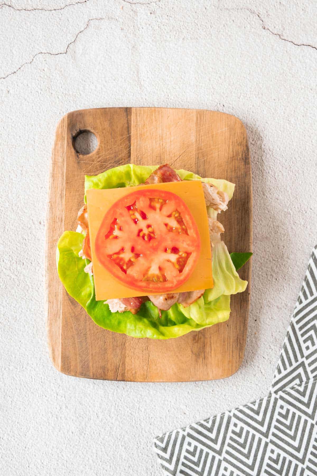 A sandwich with tomatoes and lettuce on a wooden cutting board.