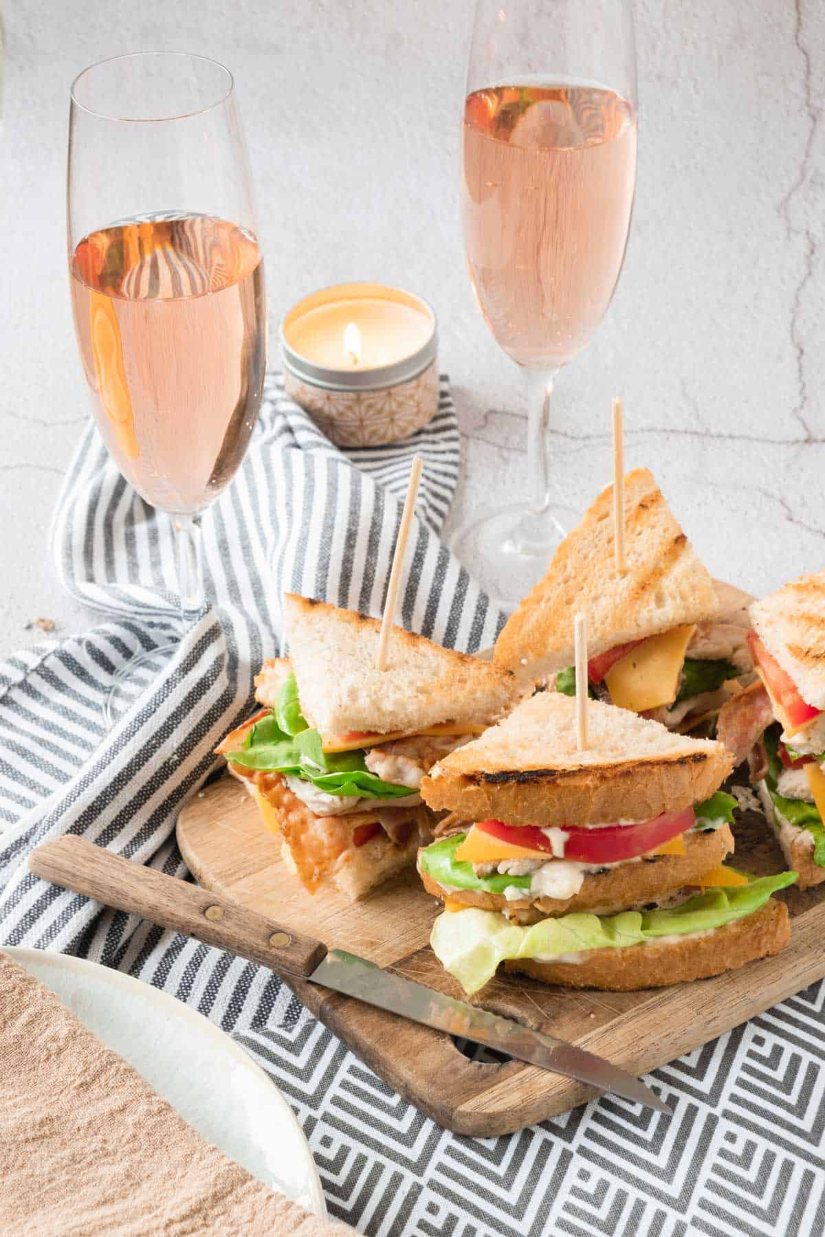 Sandwiches on a cutting board with glasses of wine.
