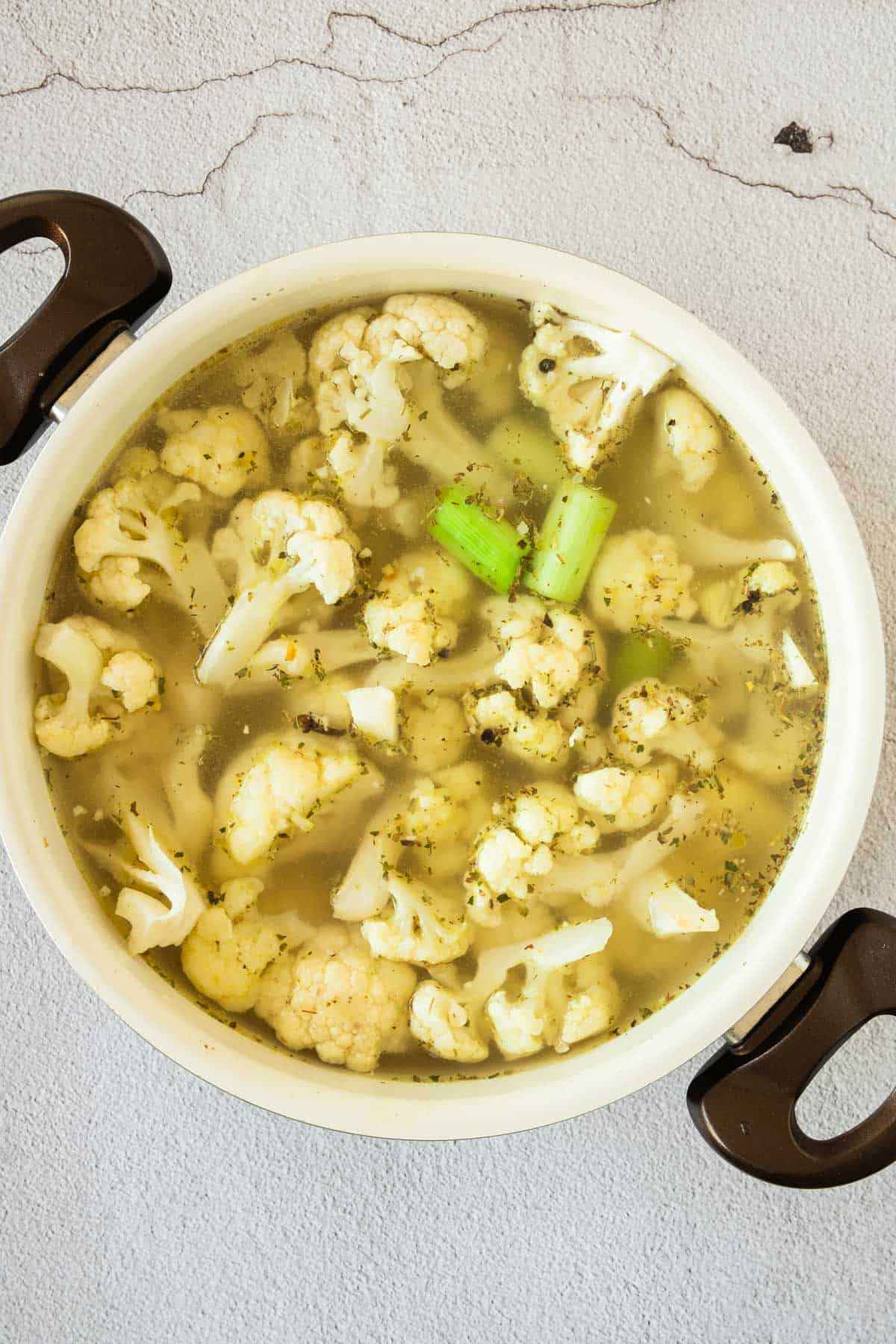 A pot with cauliflower, vegetable stock, and celery.