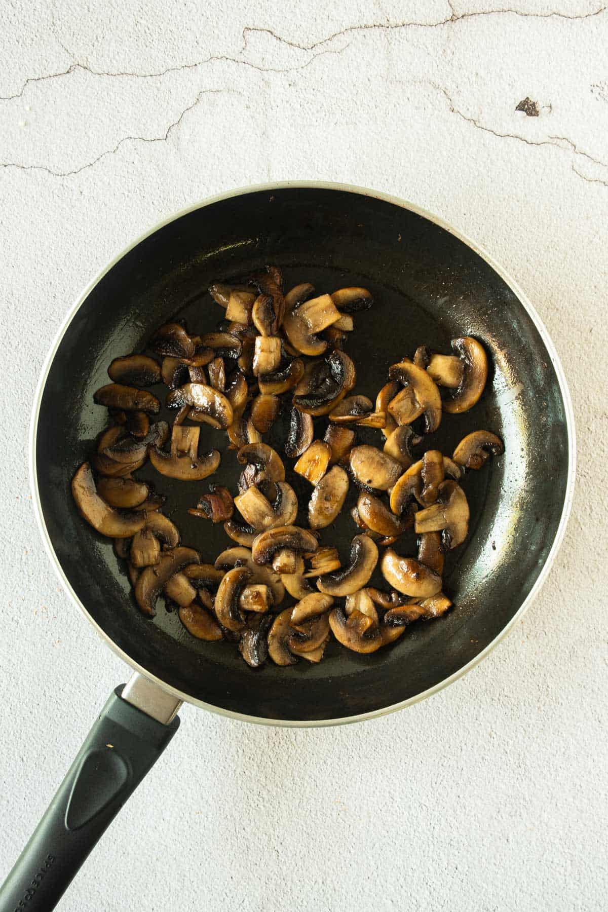 Mushrooms in a frying pan on a white surface.