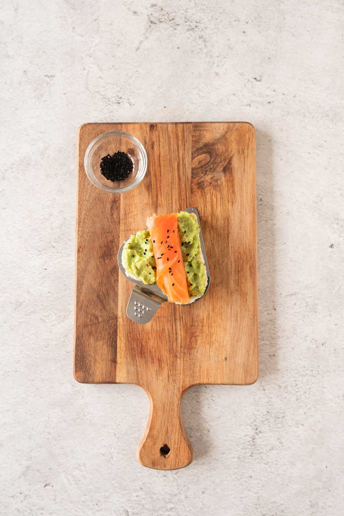 avocado and salmon sandwich on a wooden cutting board.