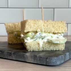 Two cucumber sandwiches with toothpicks on a slate.