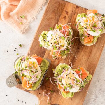 Avocado and smoked salmon heart shaped sandwich topped with sprouts on a wooden cutting board.
