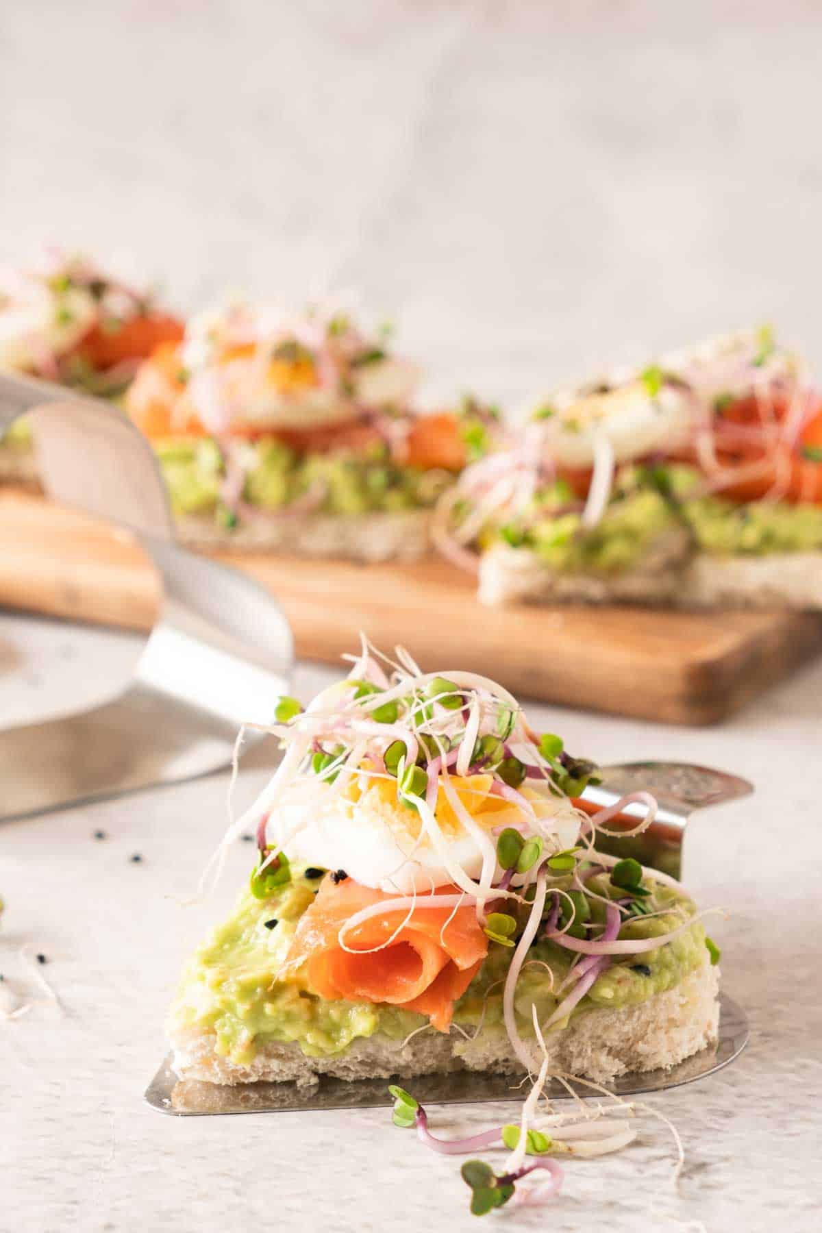 Avocado and smoked salmon heart shaped sandwich topped with sprouts on a wooden cutting board.