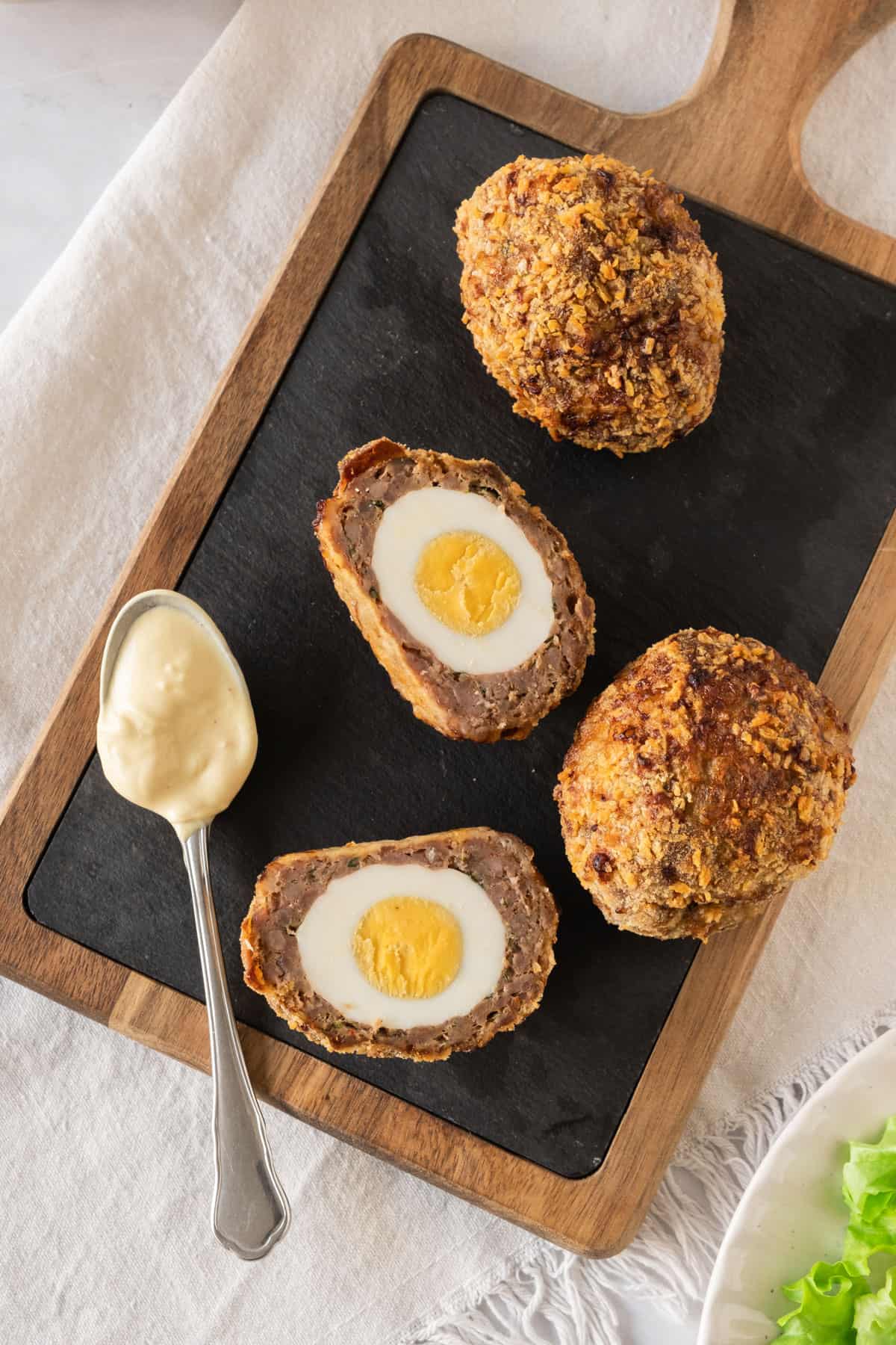 A plate with scotch eggs, one is cut in half showing the yolk. 