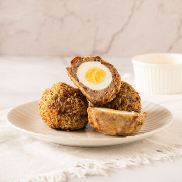 A plate with scotch eggs, one is cut in half showing the yolk.