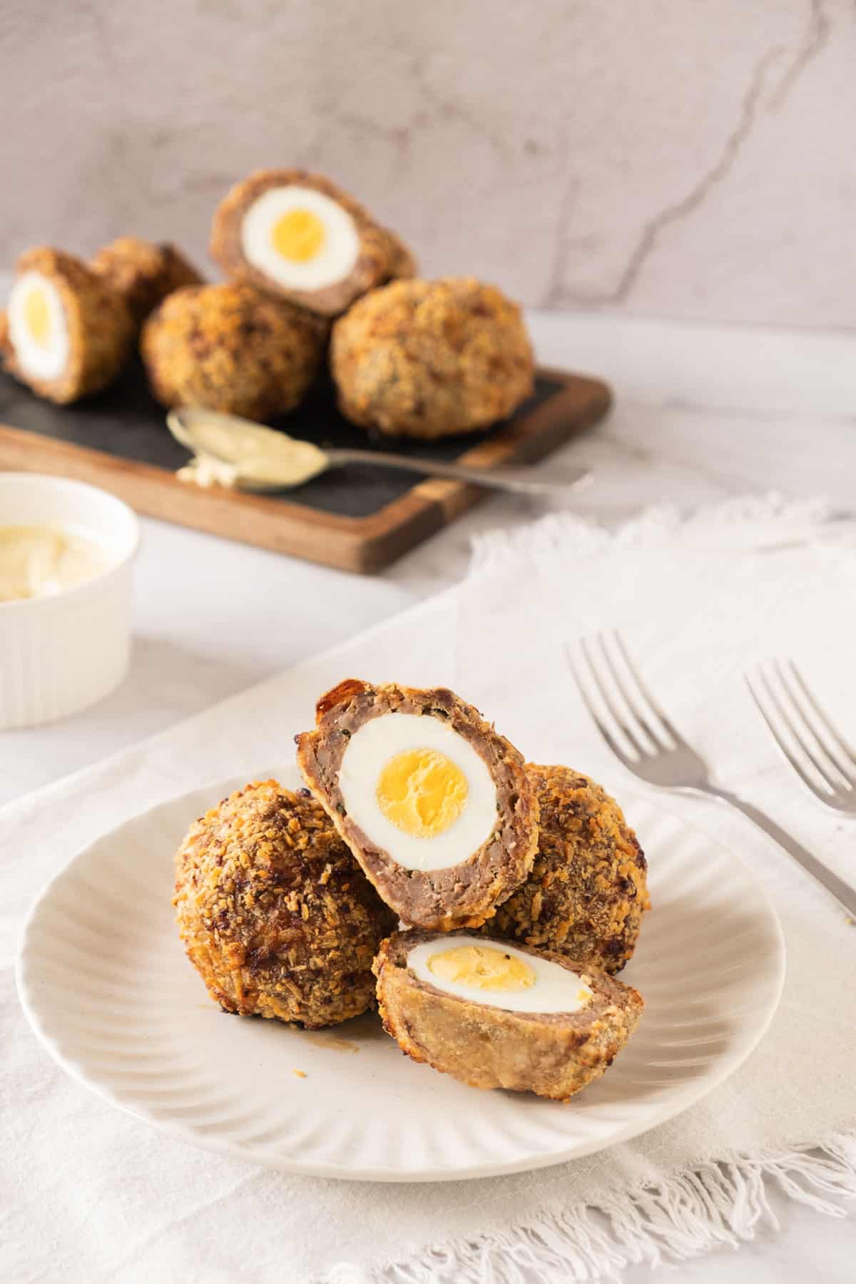 A plate with scotch eggs. Behind is a tray with more eggs. .