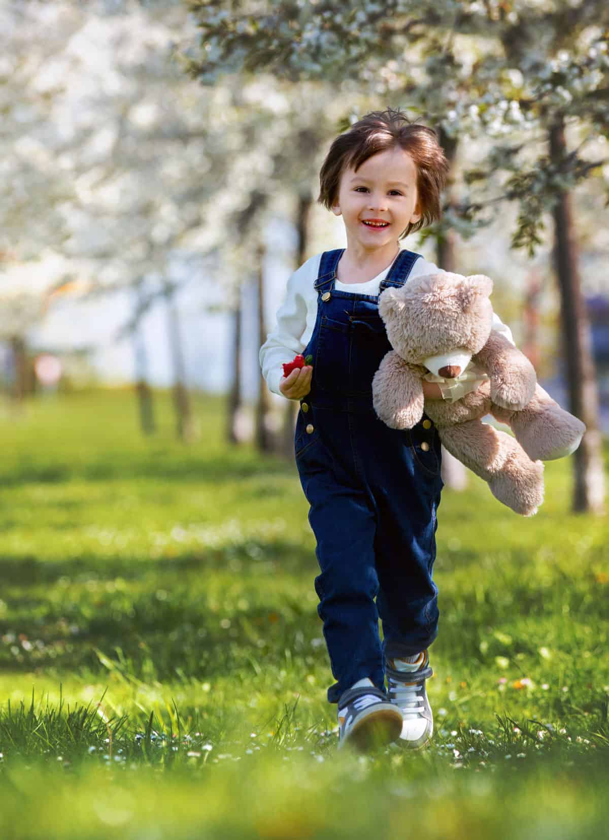 A young boy running through a field with a teddy bear.