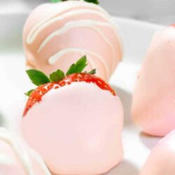 A plate of pink and white frosted strawberries on a white plate.