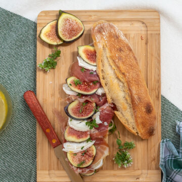 Fig and prosciutto sandwich on a wooden cutting board.