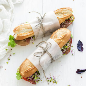 Two baguette sandwiches wrapped in paper on a wooden table.