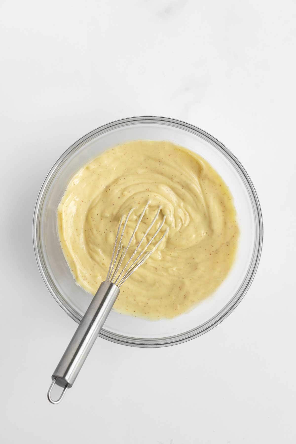 Potato salad dressing in a bowl with a whisk.