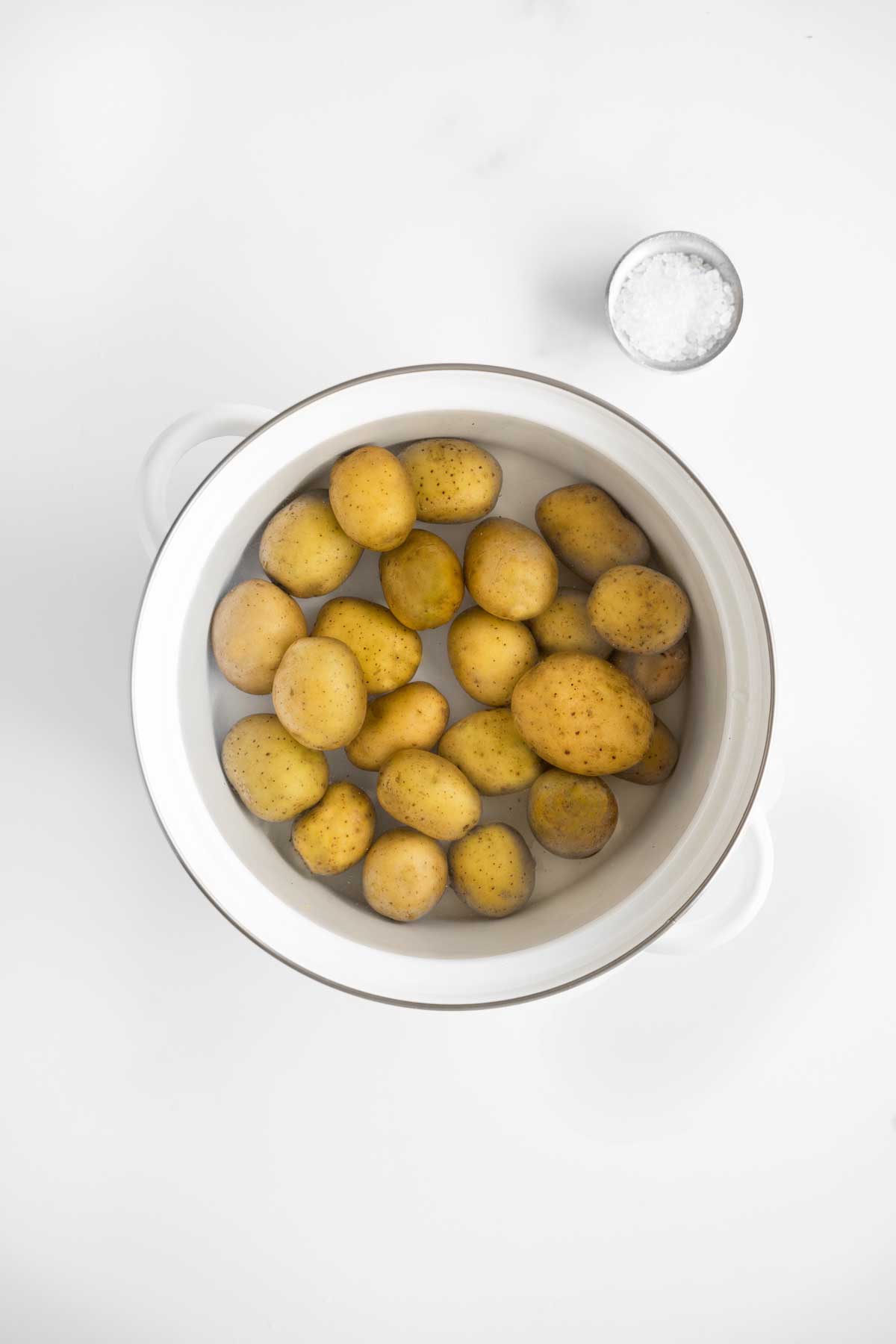 Baby potatoes in a white pot with water.