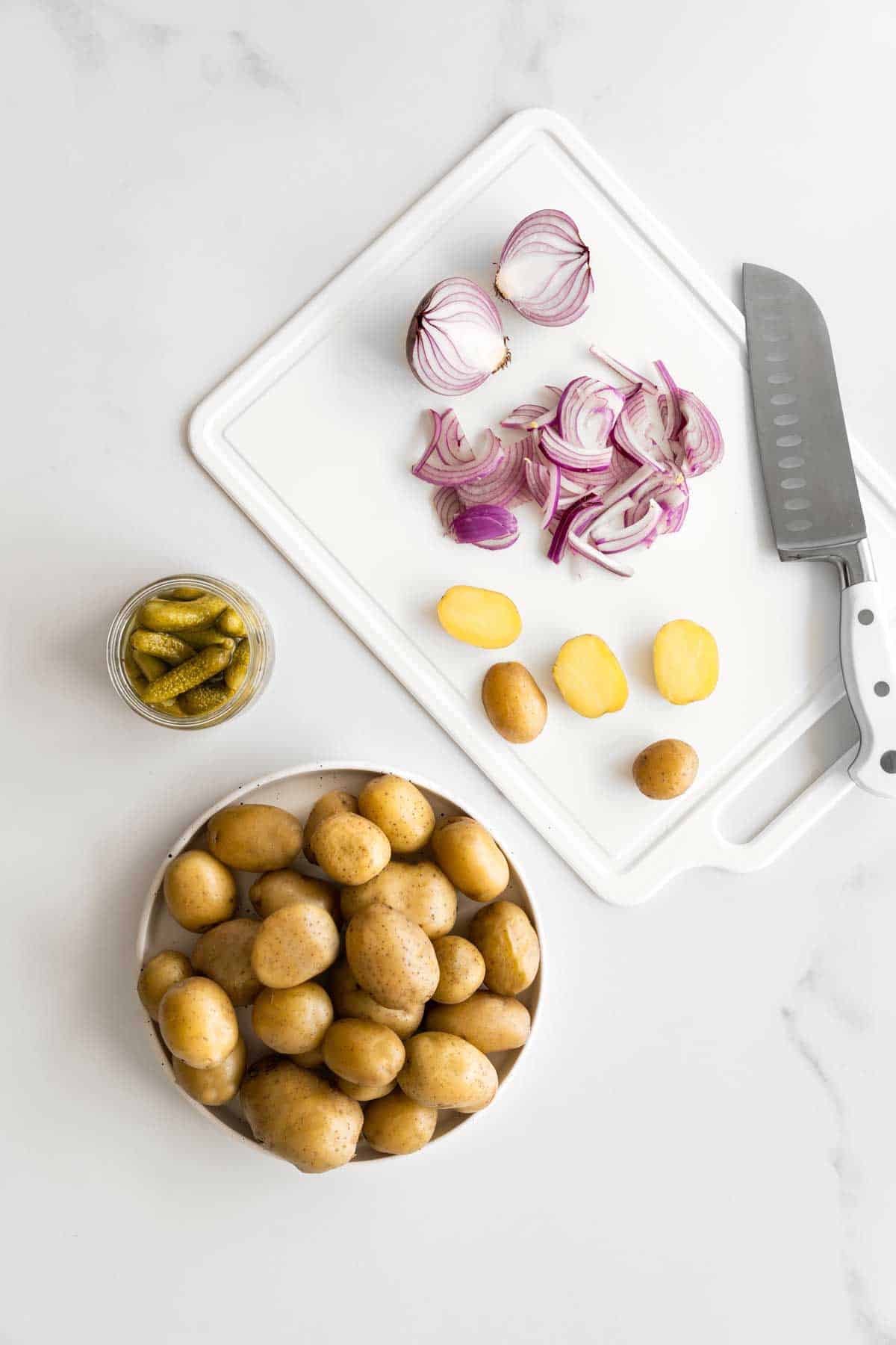 Ingredients for pickle potato salad on a chopping board with a knife.