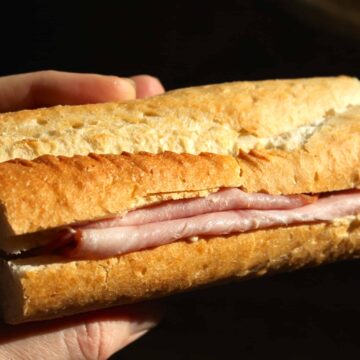 A person holding a sandwich with ham and cheese.